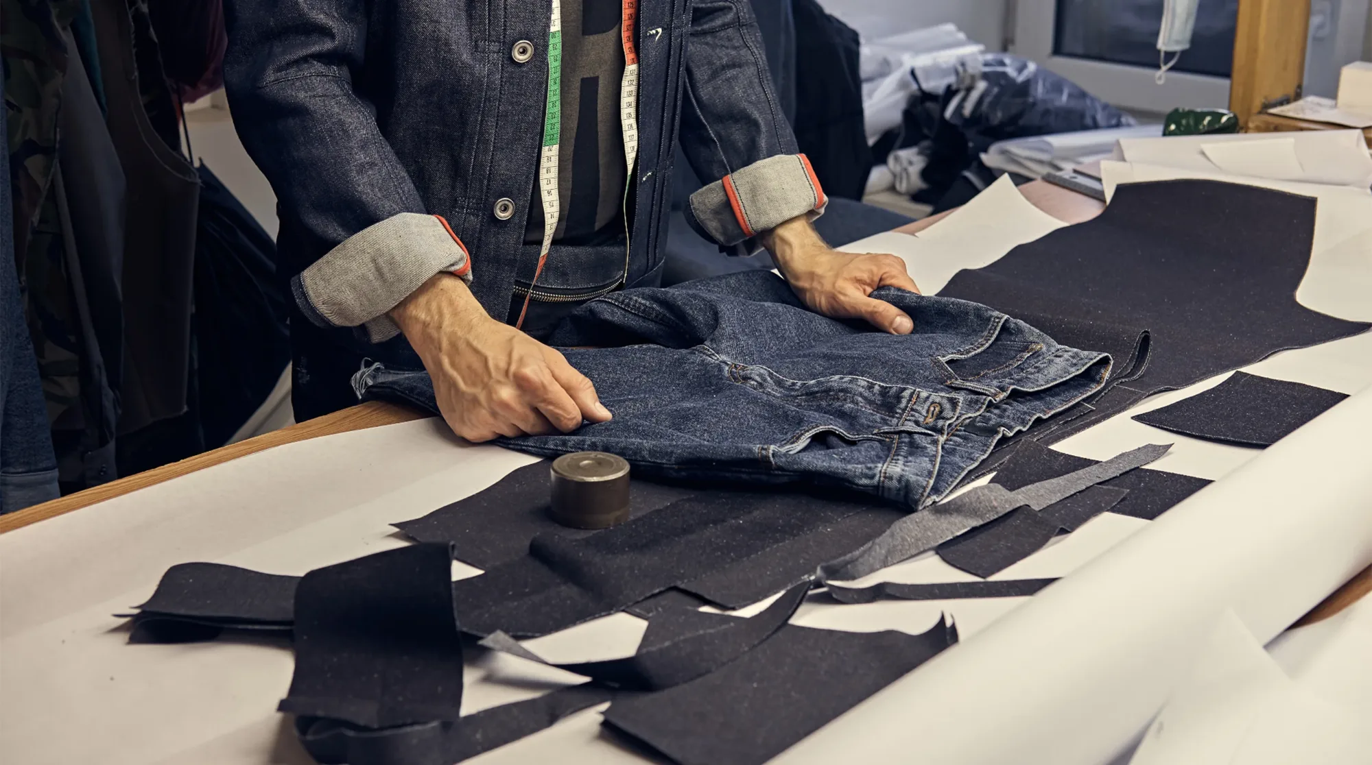 Pattern maker laying out jeans on a cutting table with cut denim pieces